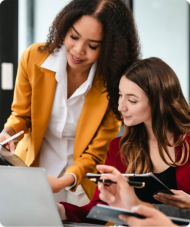 Three collaborators discussing on a tablet; one in yellow holds it, another in red takes notes